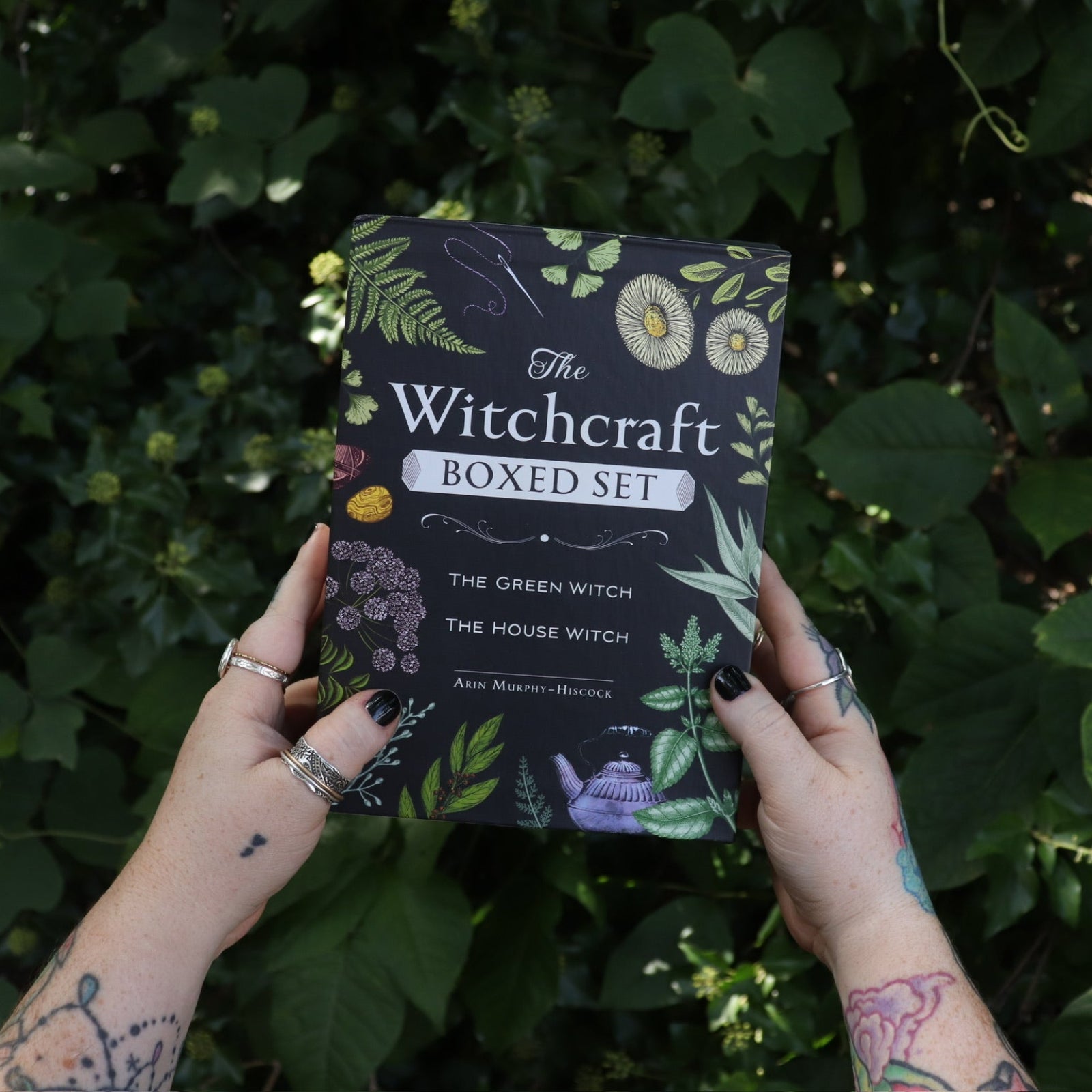 Someone holding the Witchcraft Boxed Set by Arin Murphy-Hiscock in front of greenery.