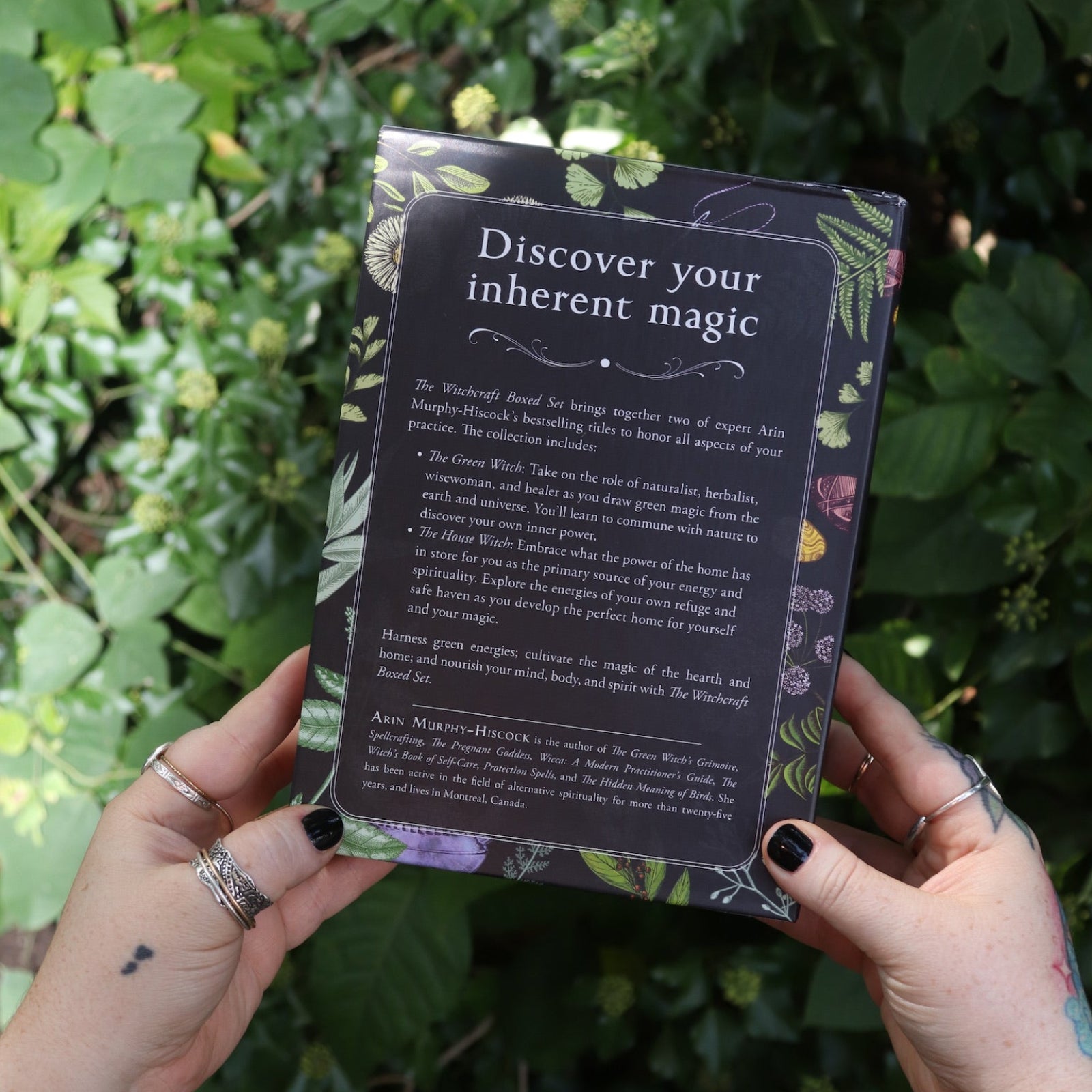 Someone holding the Witchcraft Boxed Set by Arin Murphy-Hiscock in front of greenery showing the back.