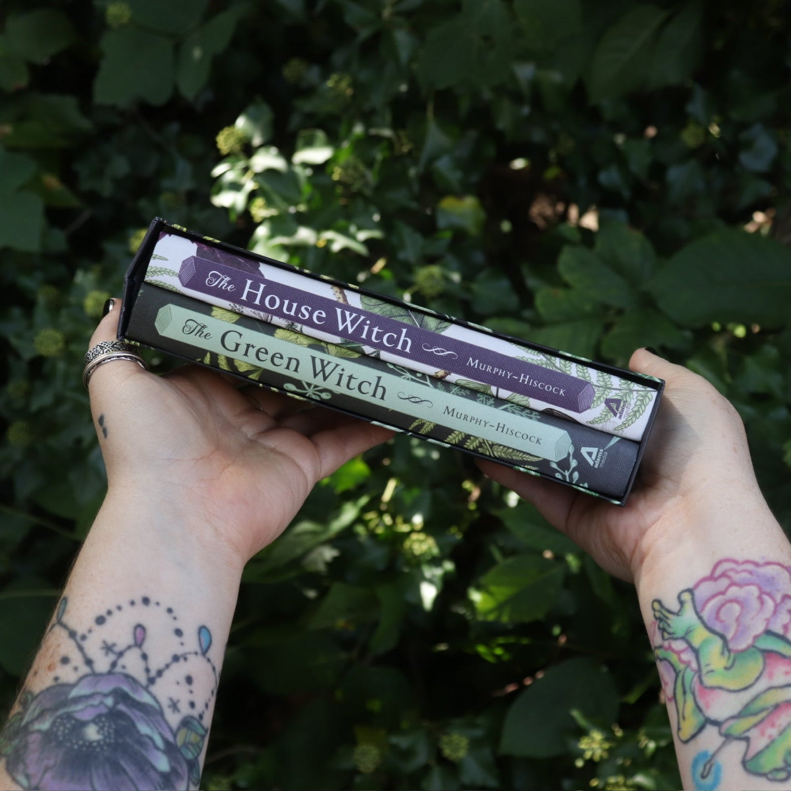 Someone holding the Witchcraft Boxed Set by Arin Murphy-Hiscock in front of greenery showing the spines of the two books.