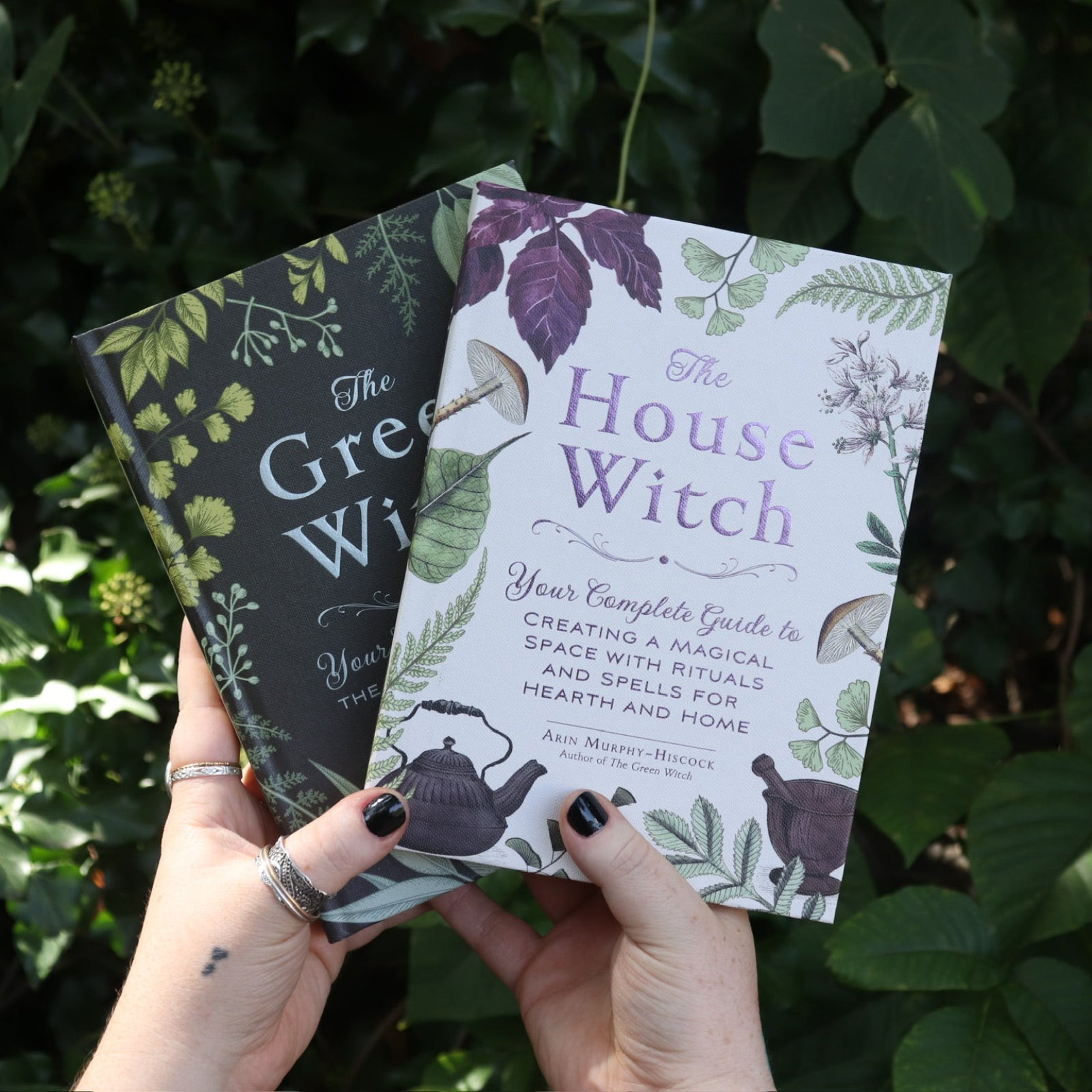 Someone holding the two books that come in the Witchcraft Boxed Set by Arin Murphy-Hiscock in front of greenery.