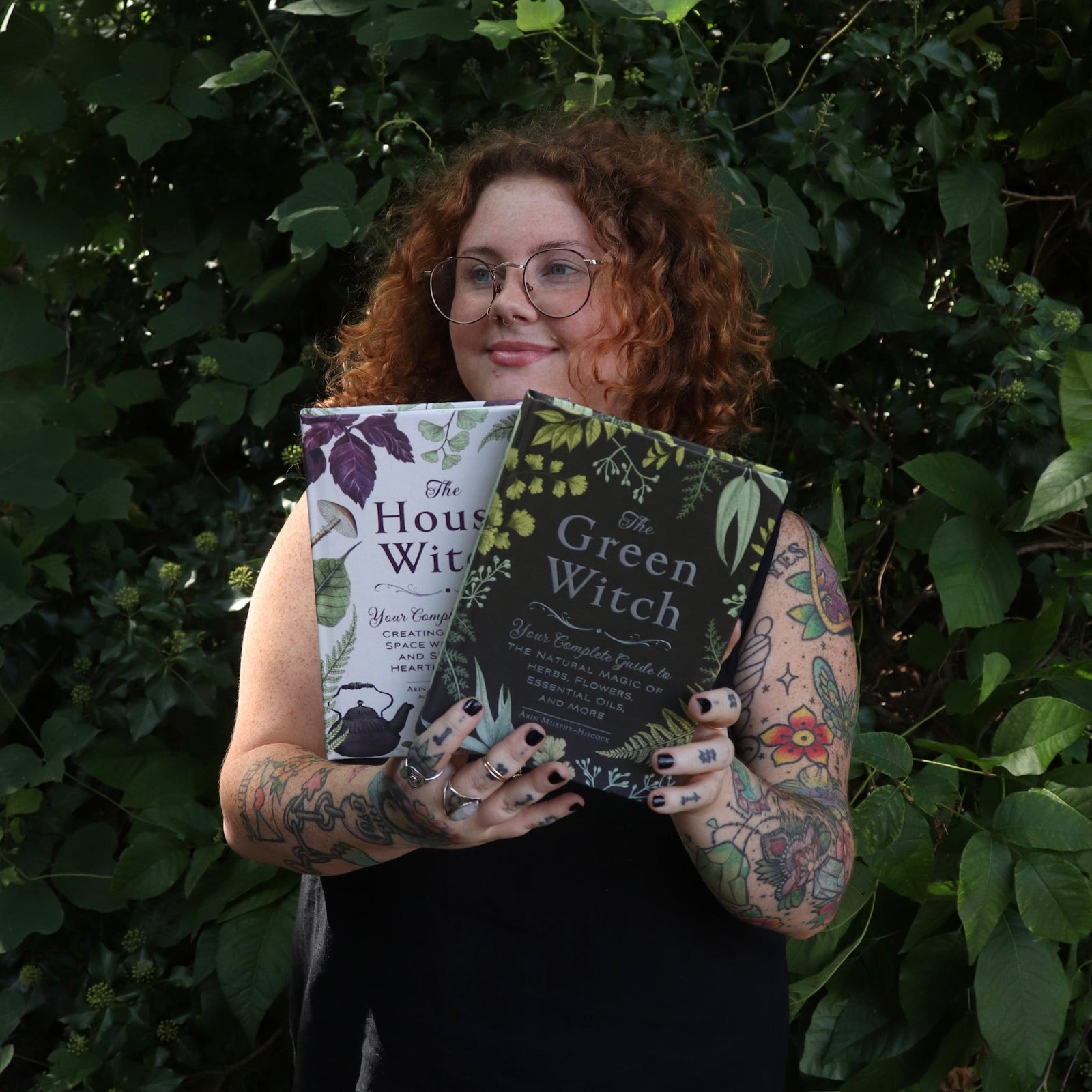A woman holding the books from the Witchcraft Boxed Set by Arin Murphy-Hiscock in front of greenery.