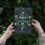 Someone holding Runes for the Green Witch by Nicolette Miele in front of greenery.