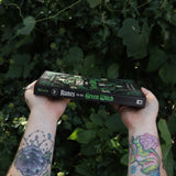 Someone holding Runes for the Green Witch by Nicolette Miele in front of greenery showing off the book's spine.