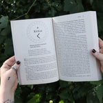 Someone holding Runes for the Green Witch by Nicolette Miele in front of greenery showing off its pages.
