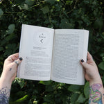 Someone holding Runes for the Green Witch by Nicolette Miele in front of greenery showing off its pages.