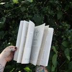 Someone holding Runes for the Green Witch by Nicolette Miele in front of greenery showing off its pages.