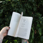 Someone holding Runes for the Green Witch by Nicolette Miele in front of greenery showing off its pages.