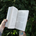 Someone holding Runes for the Green Witch by Nicolette Miele in front of greenery showing off its pages.