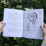 Someone holding the Tarot Coloring - Coloring Book open in front of greenery showing off pages.