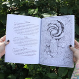 Someone holding the Tarot Coloring - Coloring Book open in front of greenery showing off pages.