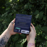 Someone holding the Pocket Book of Stones by Robert Simmons in front of greenery showing off the back