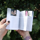 Someone holding the Pocket Book of Stones by Robert Simmons open in front of greenery to show off its pages.