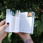 Someone holding the Pocket Book of Stones by Robert Simmons open in front of greenery to show off its pages.
