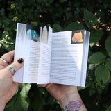 Someone holding the Pocket Book of Stones by Robert Simmons open in front of greenery to show off its pages.