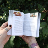 Someone holding the Pocket Book of Stones by Robert Simmons open in front of greenery to show off its pages.
