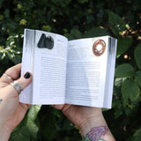 Someone holding the Pocket Book of Stones by Robert Simmons open in front of greenery to show off its pages.