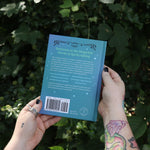 Someone holding the Spell Jars for the Modern Witch Book in front of greenery, showing off the back.