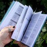 Someone holding the Spell Jars for the Modern Witch Book in front of greenery, showing off the pages.