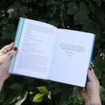 Someone holding the Spell Jars for the Modern Witch Book in front of greenery, showing off the pages.