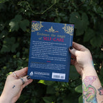 Someone holding the Witch's Book of Self-Care in front of greenery, showing off the back.