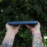 Someone holding the Witch's Book of Self-Care in front of greenery, showing off the spine.