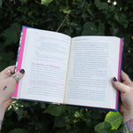Someone holding the Witch's Book of Self-Care in front of greenery, showing off the pages.