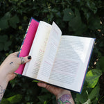 Someone holding the Witch's Book of Self-Care in front of greenery, showing off the pages.