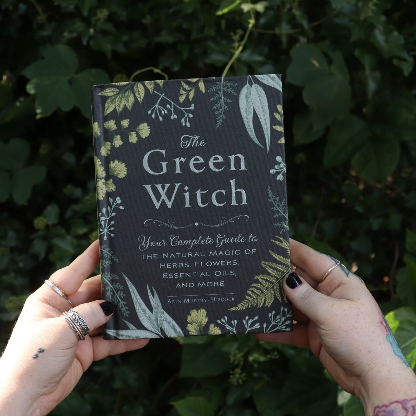 Someone holding the Green Witch by Arin Murphy-Hiscock in front of greenery.