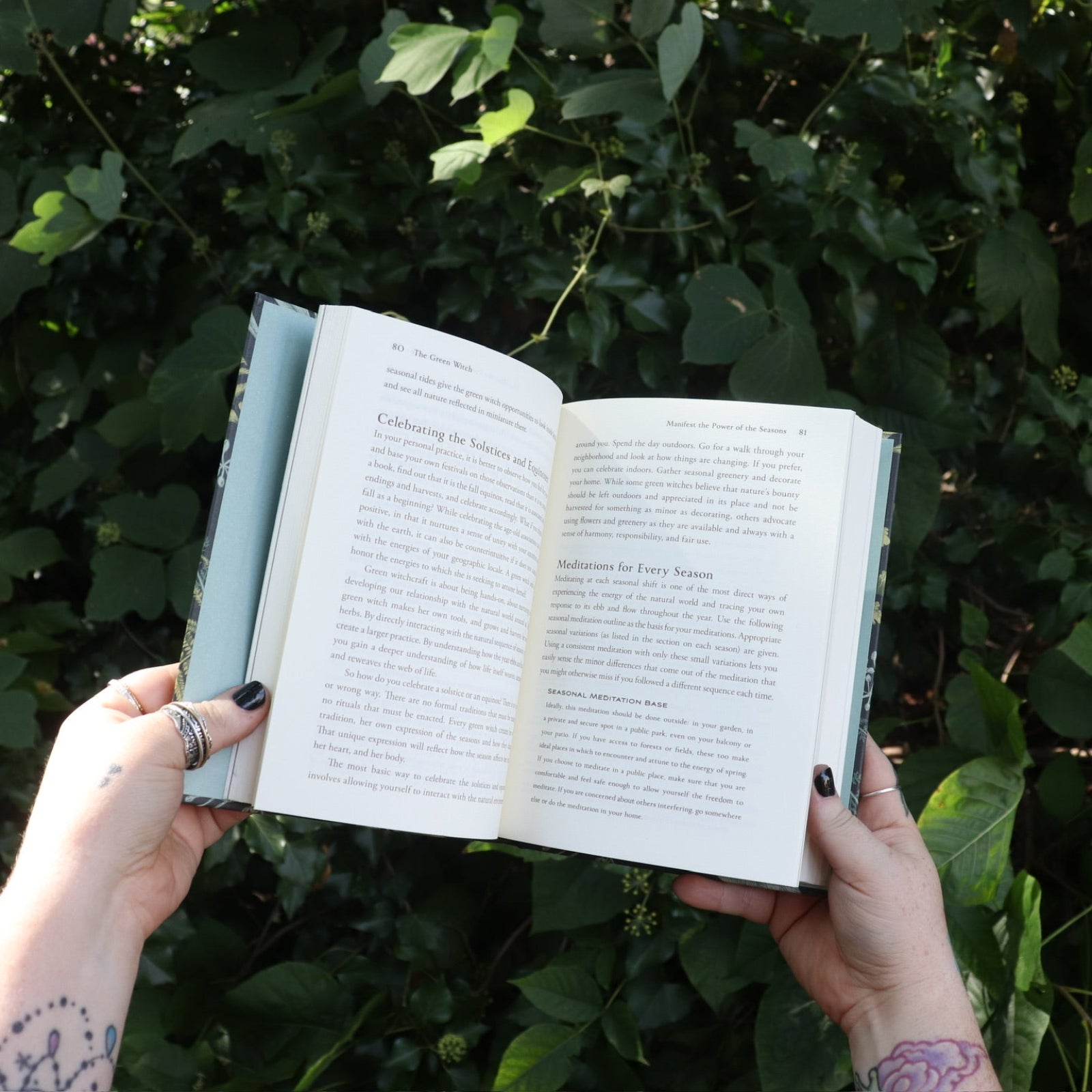 Someone holding the Green Witch by Arin Murphy-Hiscock open in front of greenery, showing off the pages.