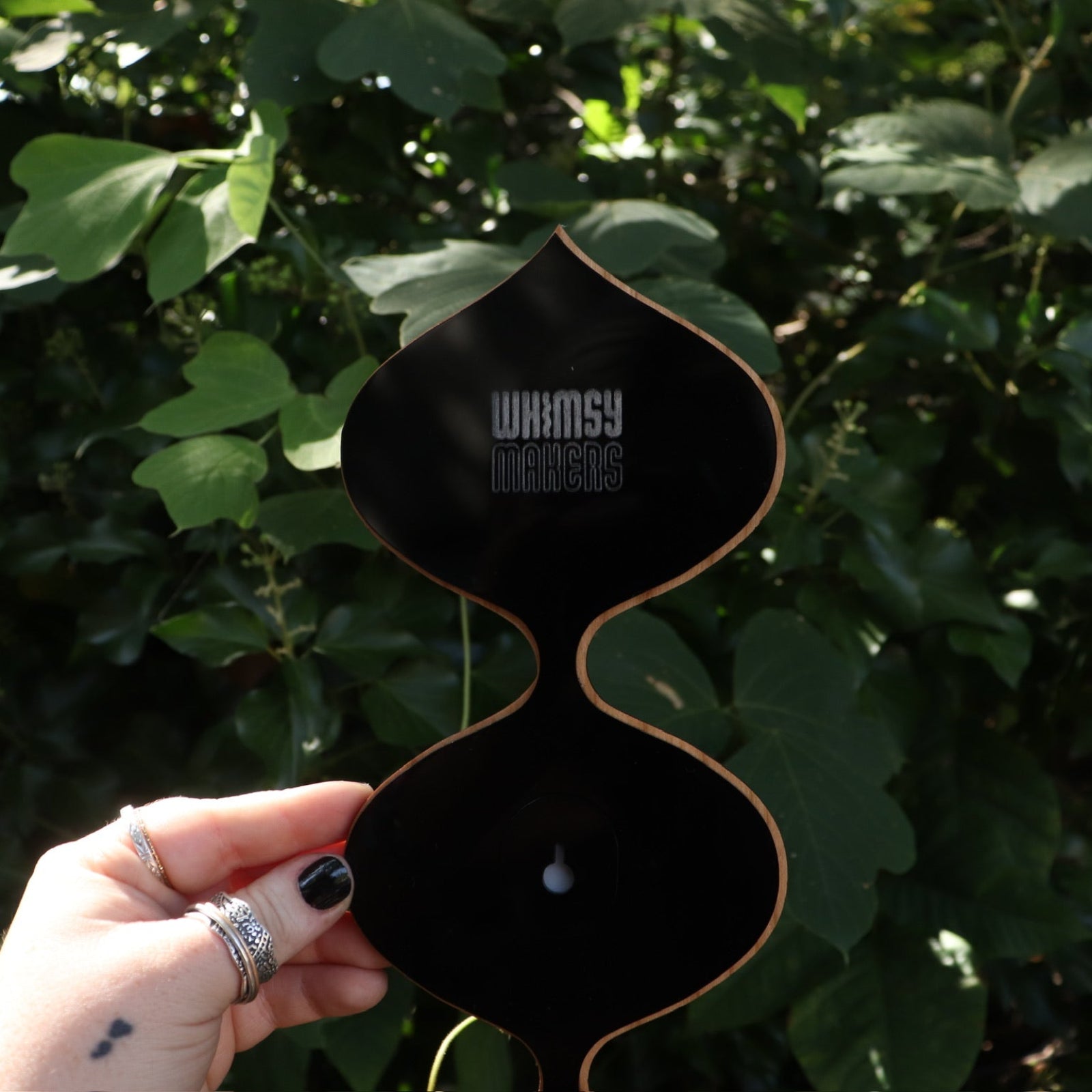 Someone holding the Retro Tear Drop Acrylic Mirror in front of greenery, showing off the back.