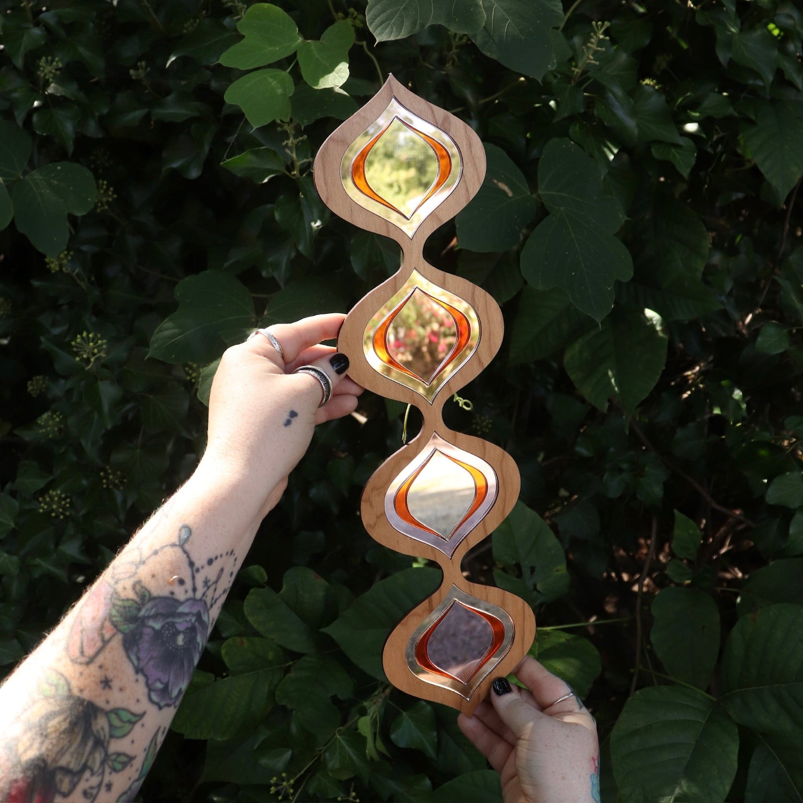 Someone holding the Retro Tear Drop Acrylic Mirror in front of greenery.