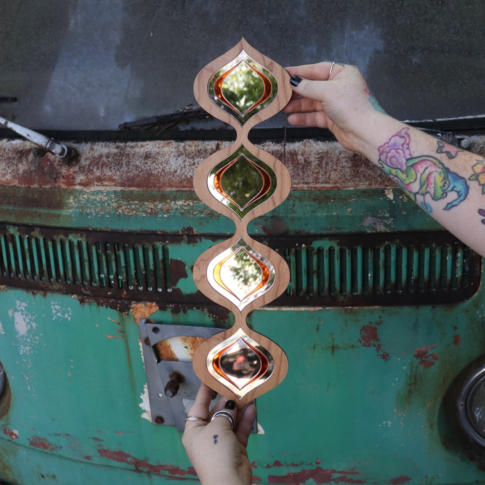 Someone holding the Retro Tear Drop Acrylic Mirror in front of a rusted vintage Volkswagen bus.