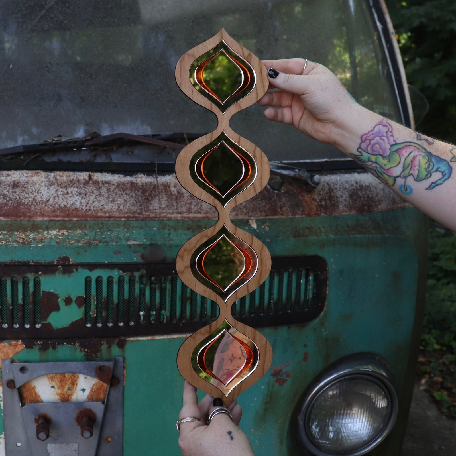 Someone holding the Retro Tear Drop Acrylic Mirror in front of a rusted vintage Volkswagen bus.