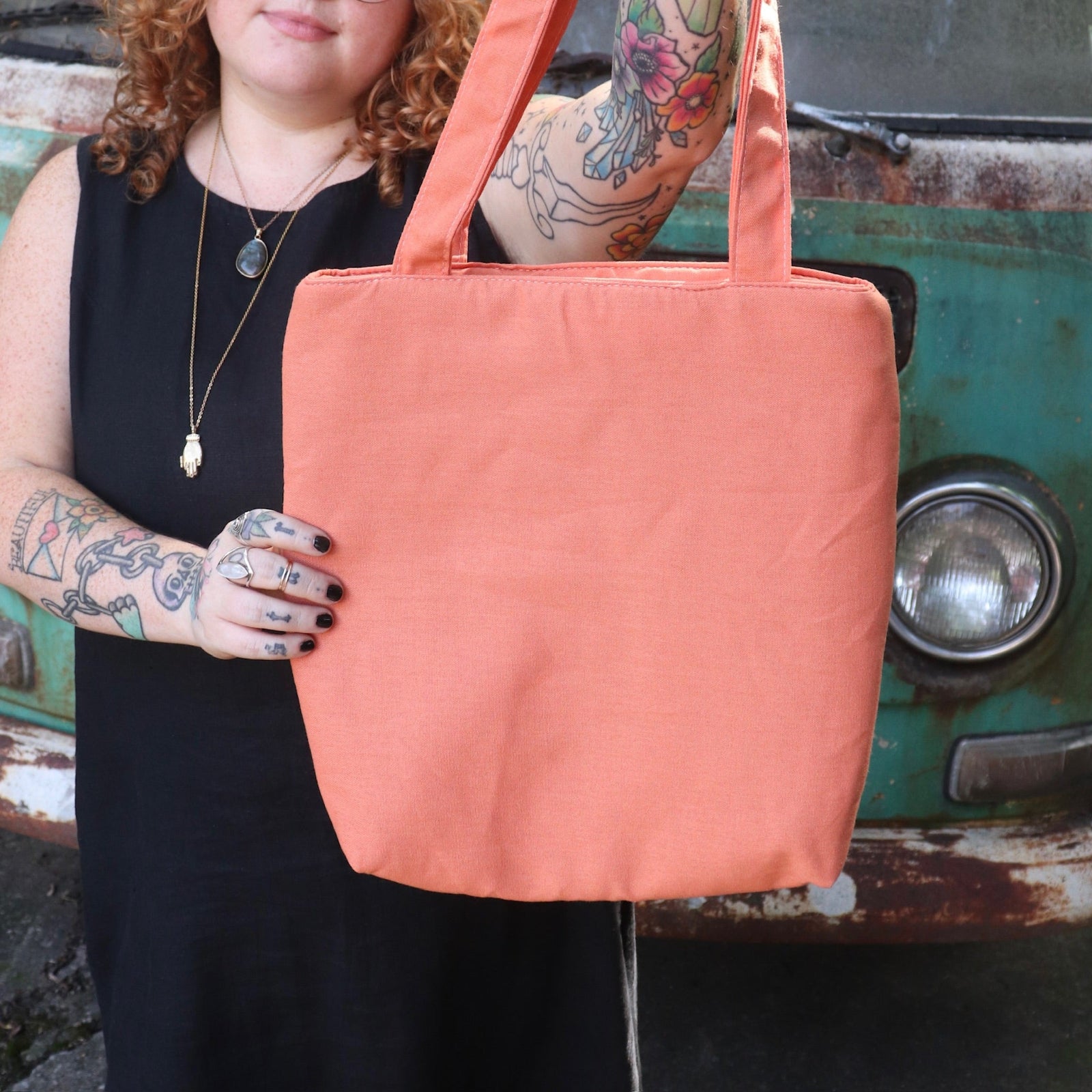 A woman holding the Daisy Embroidered Orange Linen Zipper Tote Bag while wearing a black tank dress.