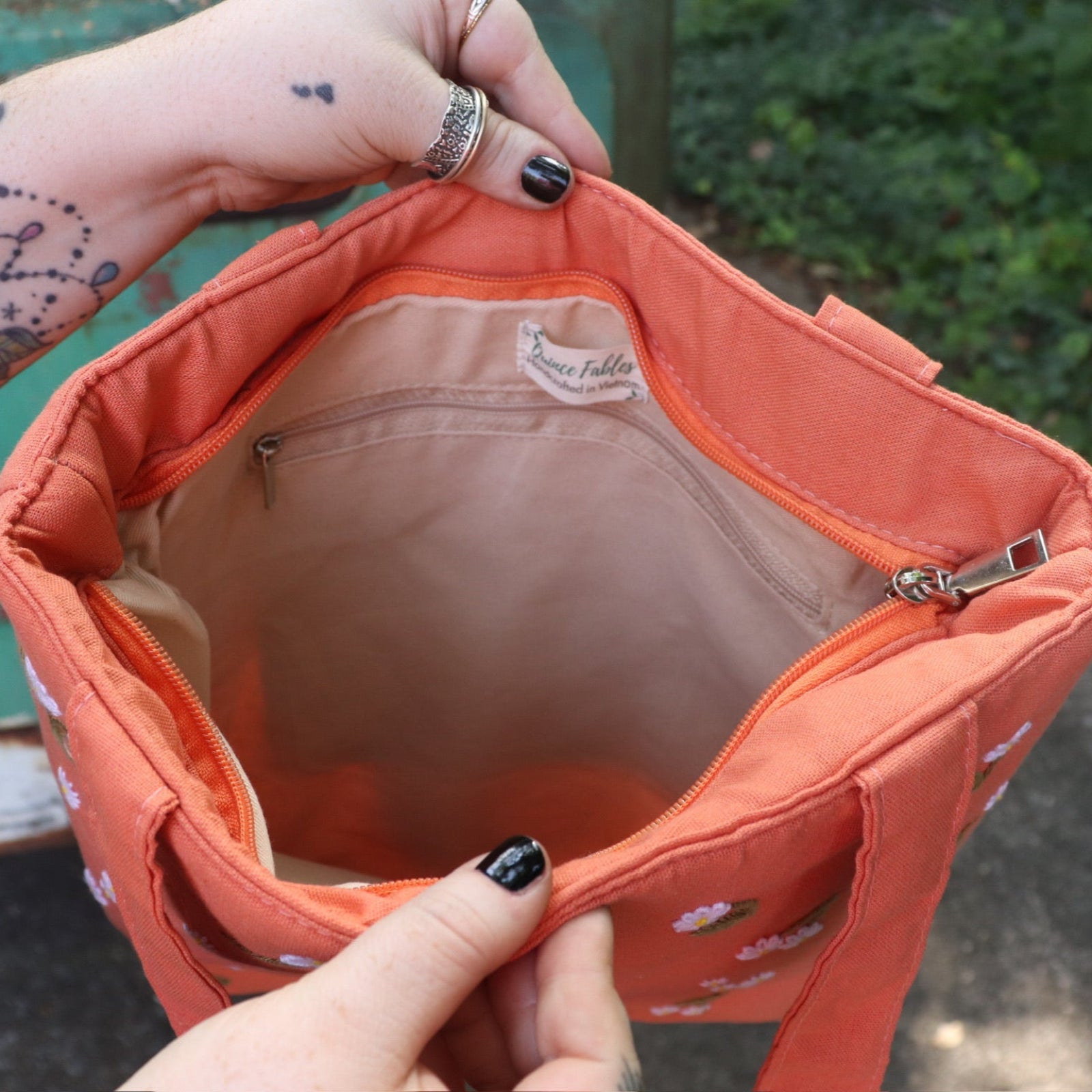 A woman holding the Daisy Embroidered Orange Linen Zipper Tote Bag open showing off the inside.