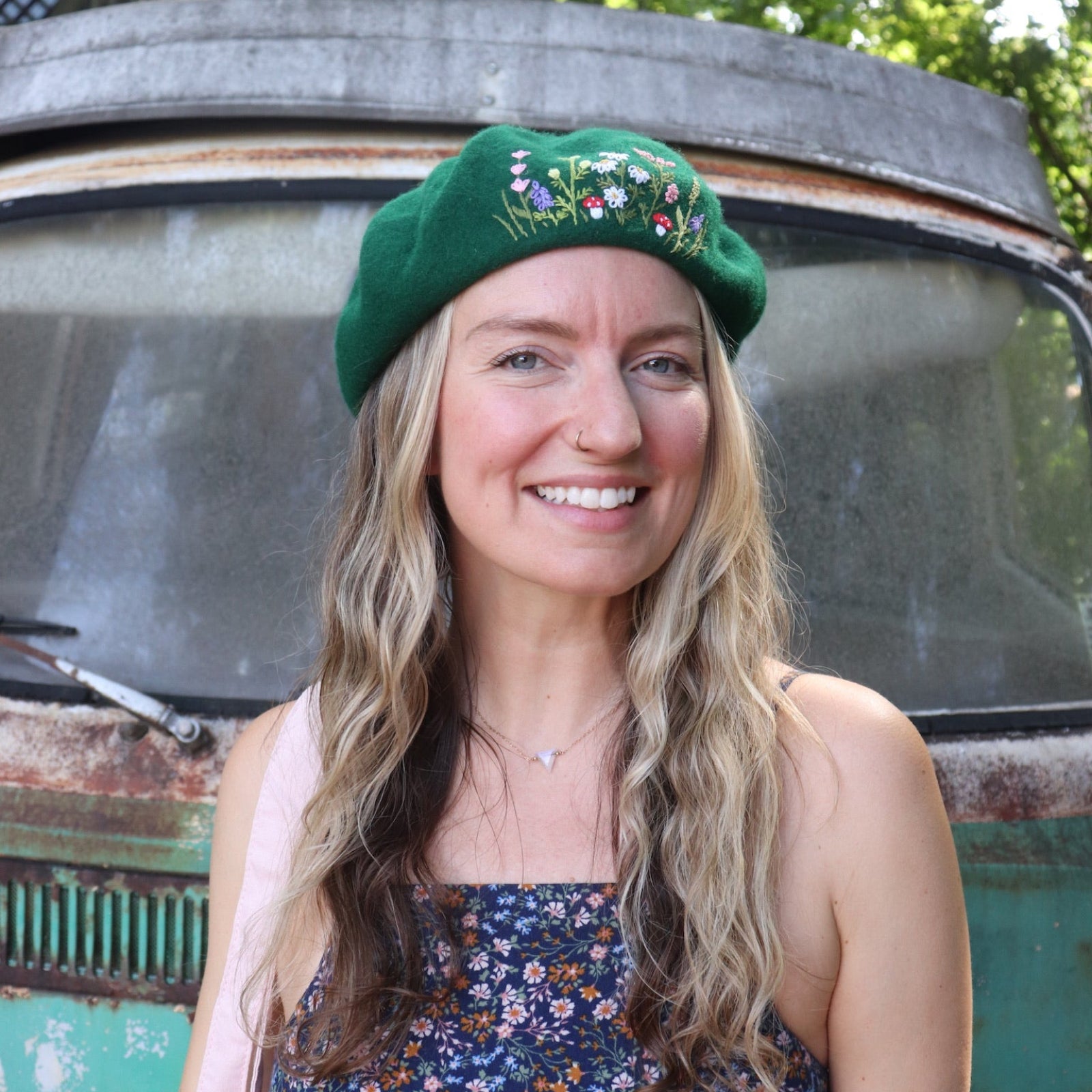 A woman wearing the green Hand-Embroidered Floral Soft Beret Stylish Hat with a navy floral dress.