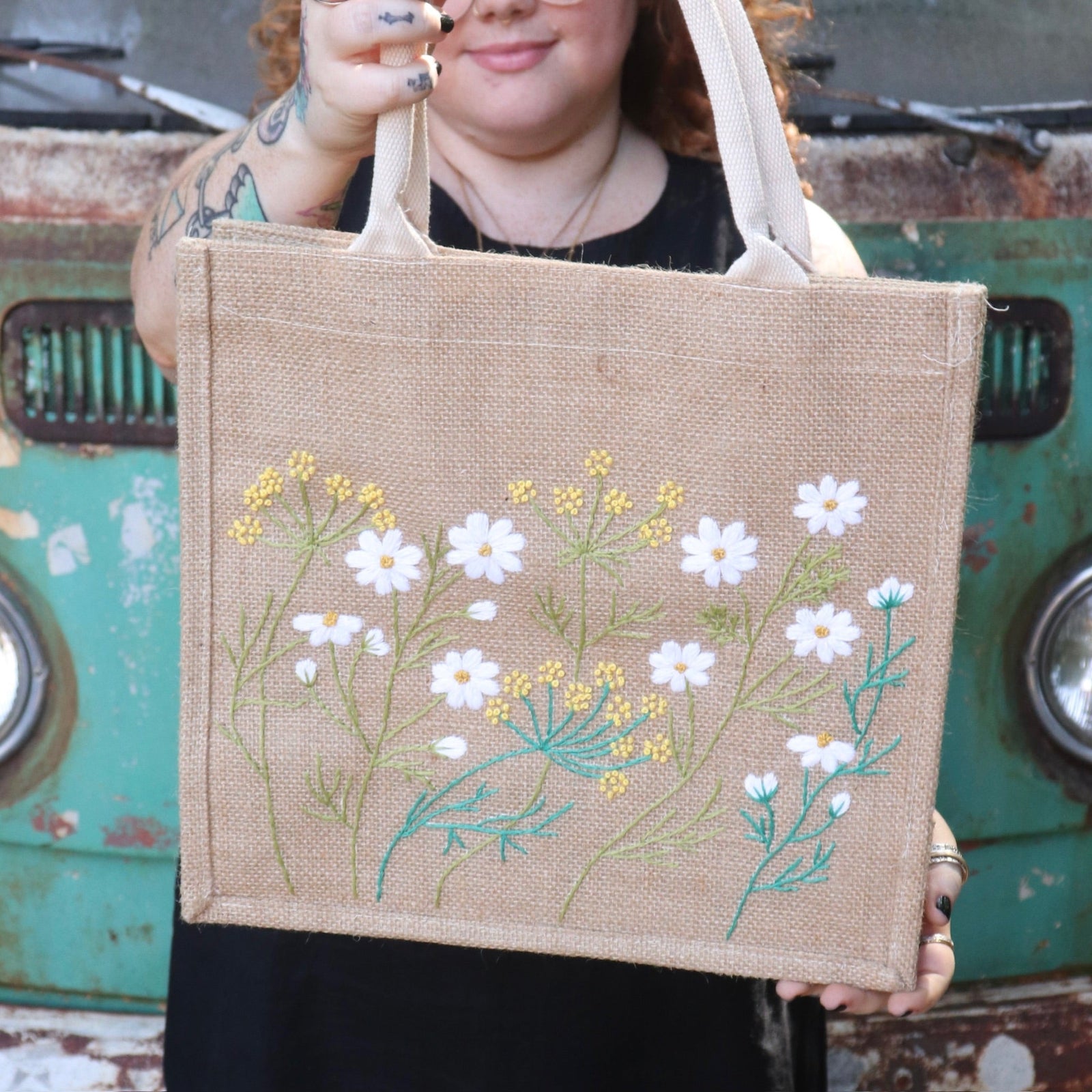 A woman wearing a black tank dress holding the Daisy Garden Embroidered Jute Bag.