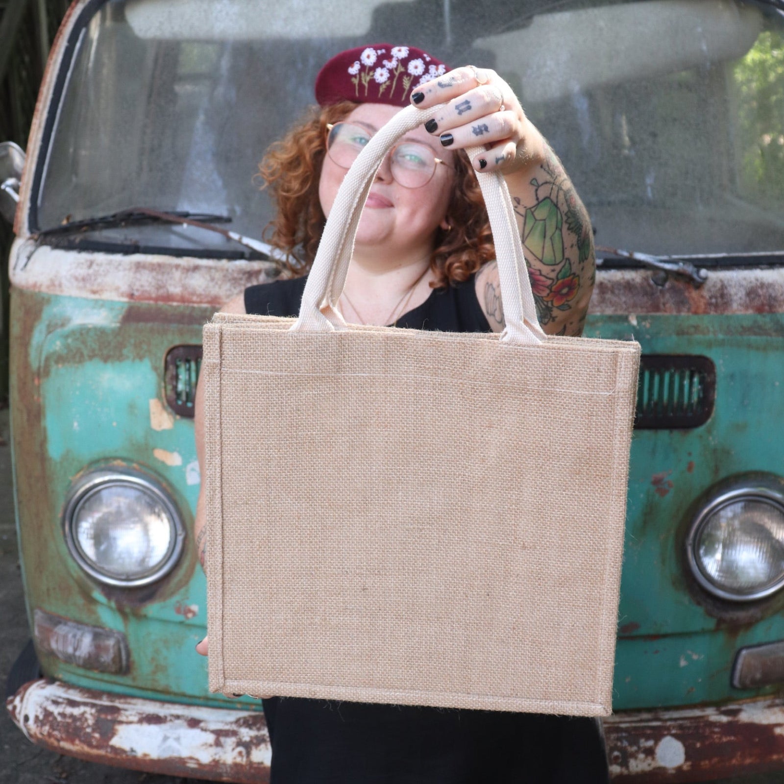 A woman wearing a black tank dress holding the Daisy Garden Embroidered Jute Bag, showing off the back.