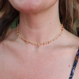 A woman wearing the orange Midsummer Gemstone Agate Gold Plated Necklace in front of some greenery.