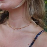 A woman wearing the orange Midsummer Gemstone Agate Gold Plated Necklace in front of some greenery.
