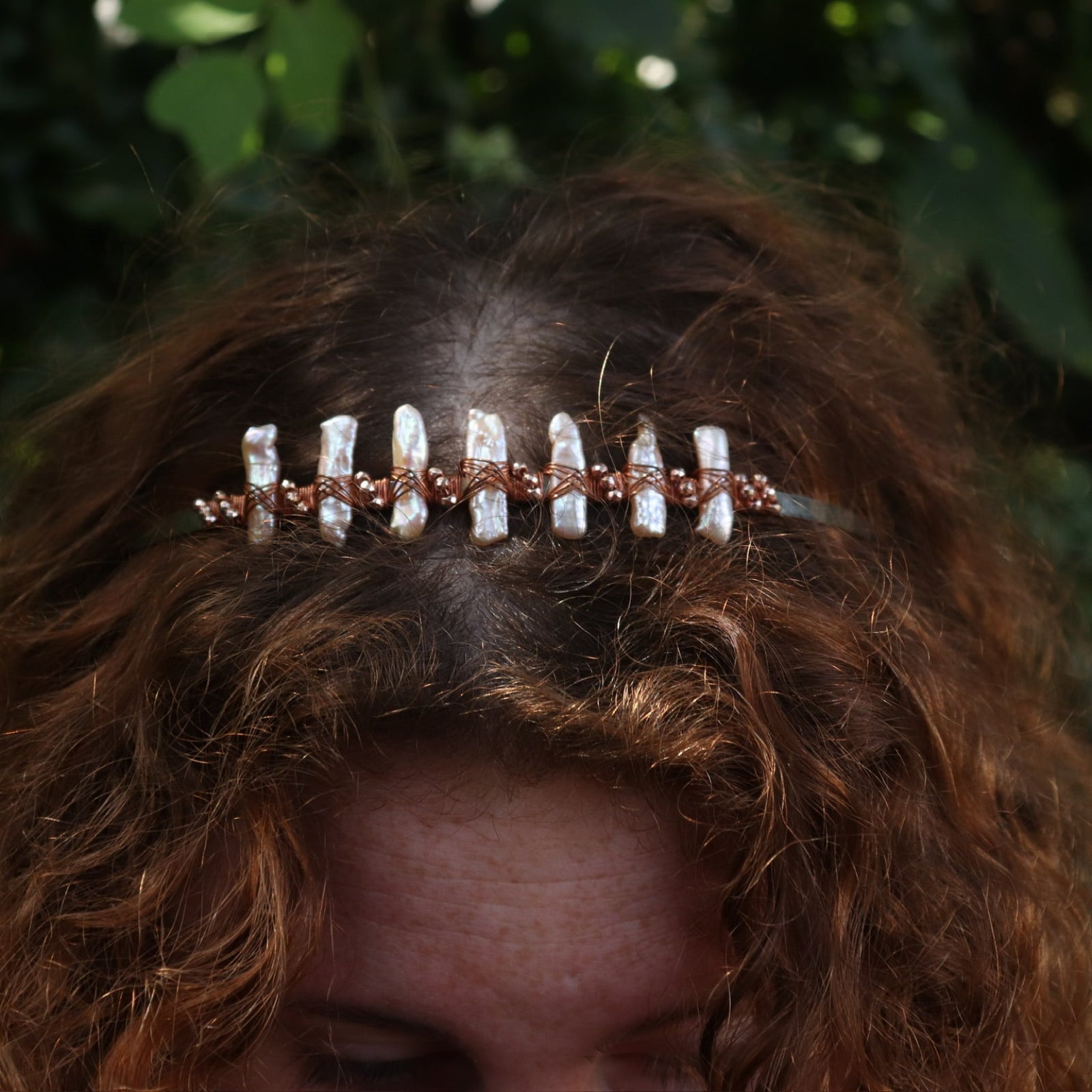 A red headed women wearing the Bridal Tiara - Rose Gold Hematite & Freshwater Pearl in front of greenery.