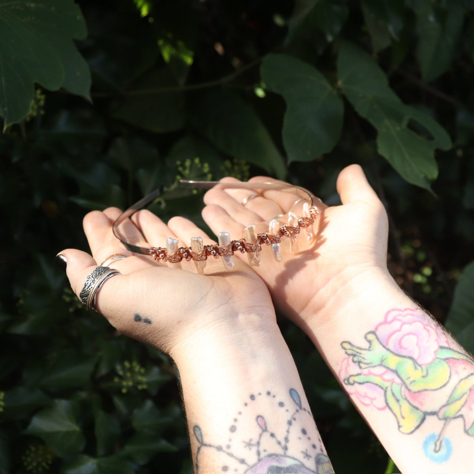Someone holding the Bridal Tiara - Rose Gold Hematite & Freshwater Pearl in front of greenery.