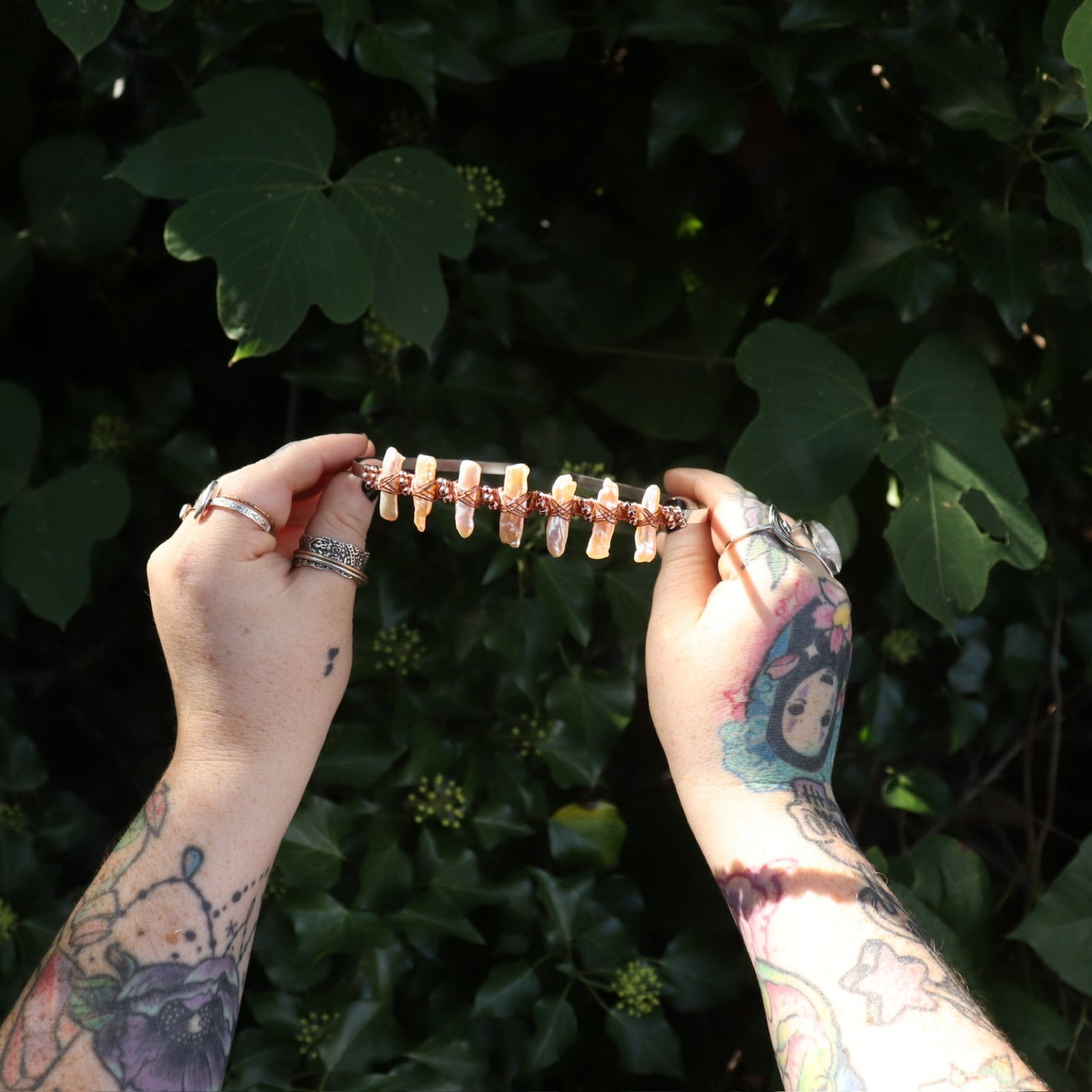 Someone holding the Bridal Tiara - Rose Gold Hematite & Freshwater Pearl in front of greenery.