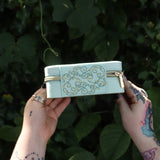 Someone holding the Once Upon a Time Travel Jewelry Organizer in front of greenery, showing off the side.