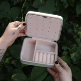 Someone holding the Once Upon a Time Travel Jewelry Organizer open in front of greenery, showing off the inside.