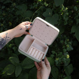 Someone holding the Once Upon a Time Travel Jewelry Organizer open in front of greenery, showing off the inside.