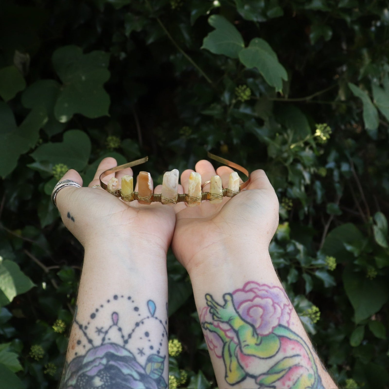 Someone holding the Fairy Crown / Celtic Tiara - Peruvian Yellow Opal in front of greenery.