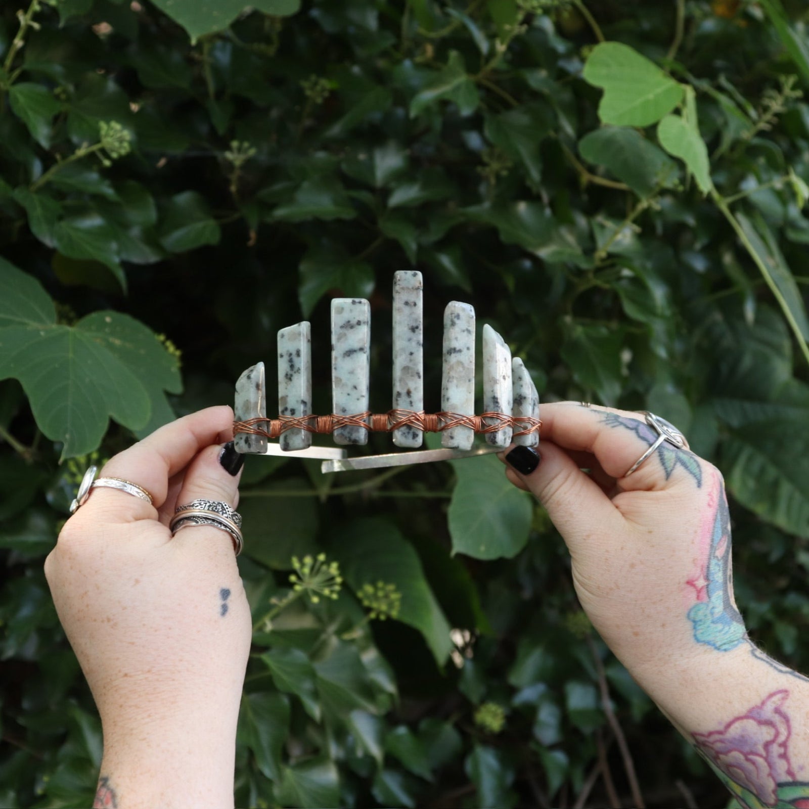 A woman holding the Gemstone Tiara / Crown - Kiwi Jasper - Sesame in front of greenery.
