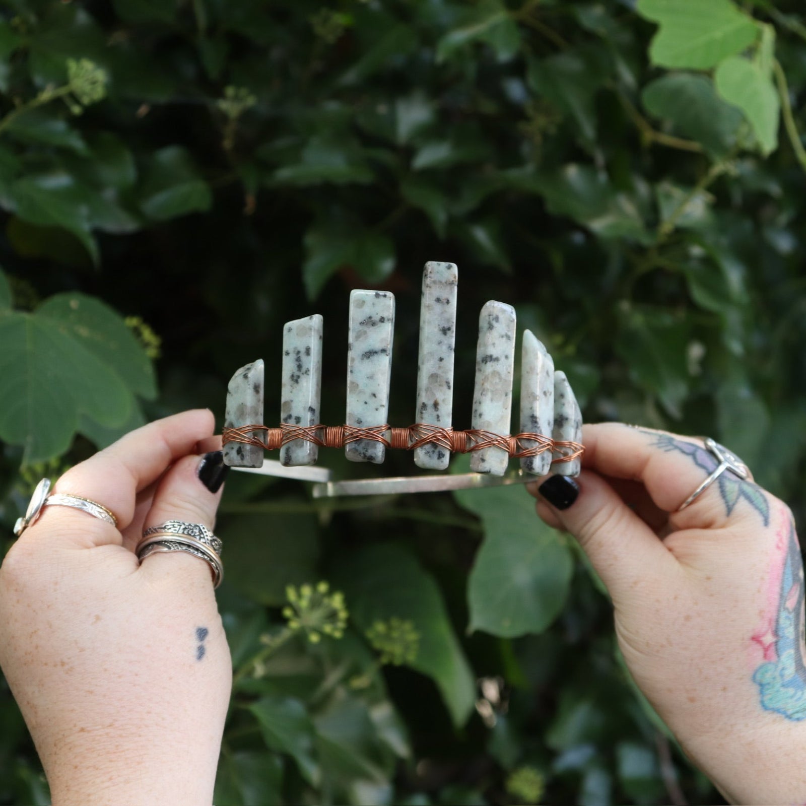 A woman holding the Gemstone Tiara / Crown - Kiwi Jasper - Sesame in front of greenery.