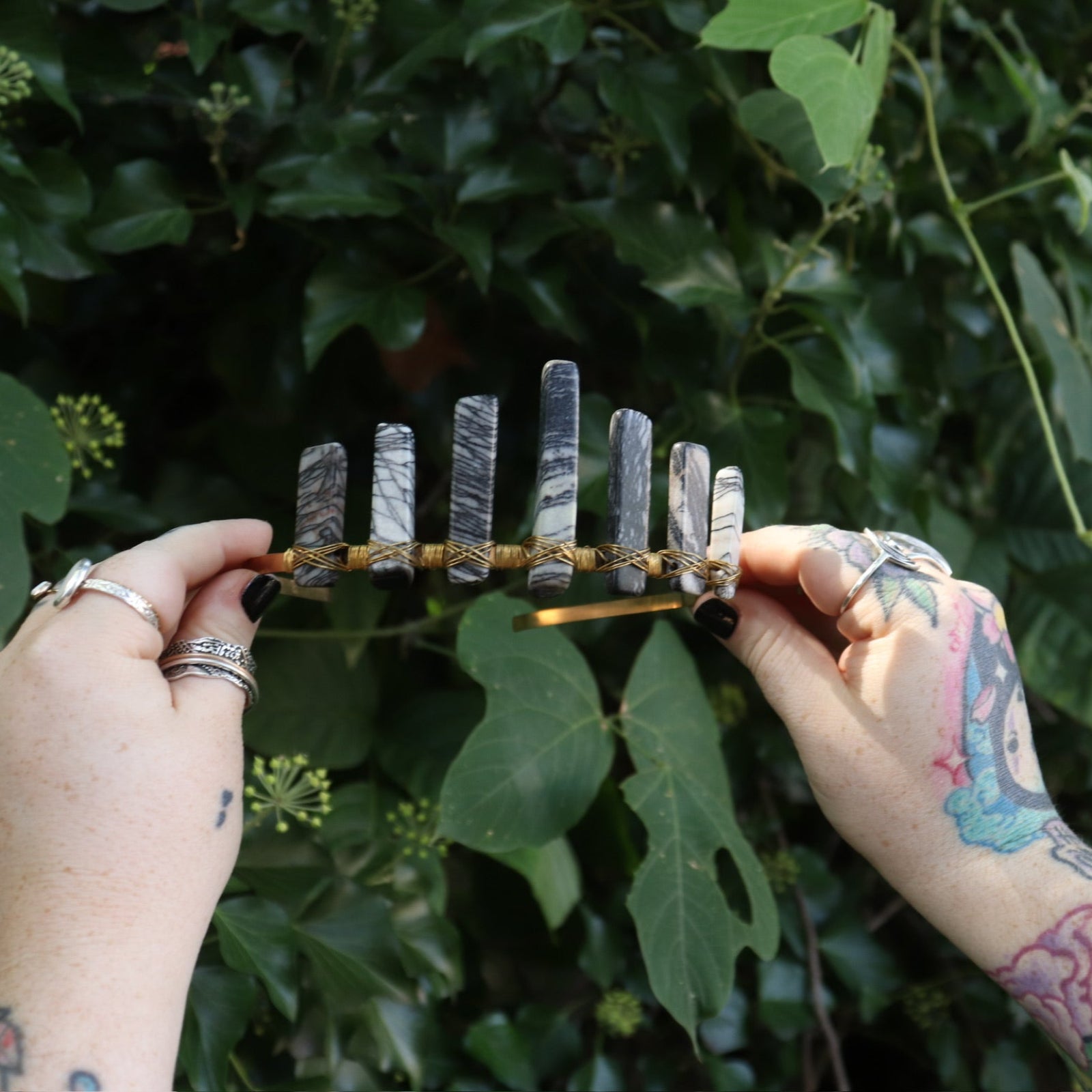 Someone holding the Fairy Crown / Celtic Tiara - Black Line Jasper - Spiderweb in front of greenery.